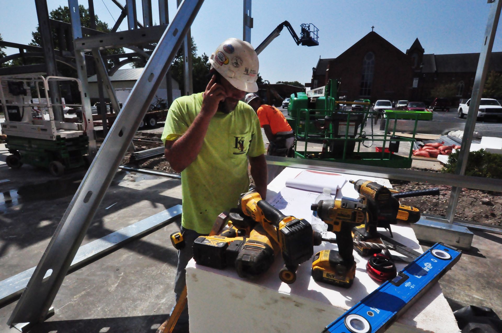 Man and woman in red shirts near a Kubota KX052 excavator. Woman sits in cab, man stands with hand on hip. Outdoors.