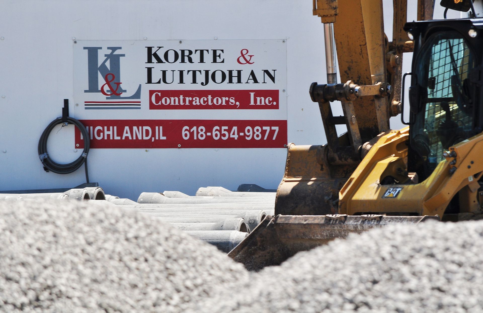 Excavator next to a sign for Korte & Luitjohan Contractors in Highland, IL.
