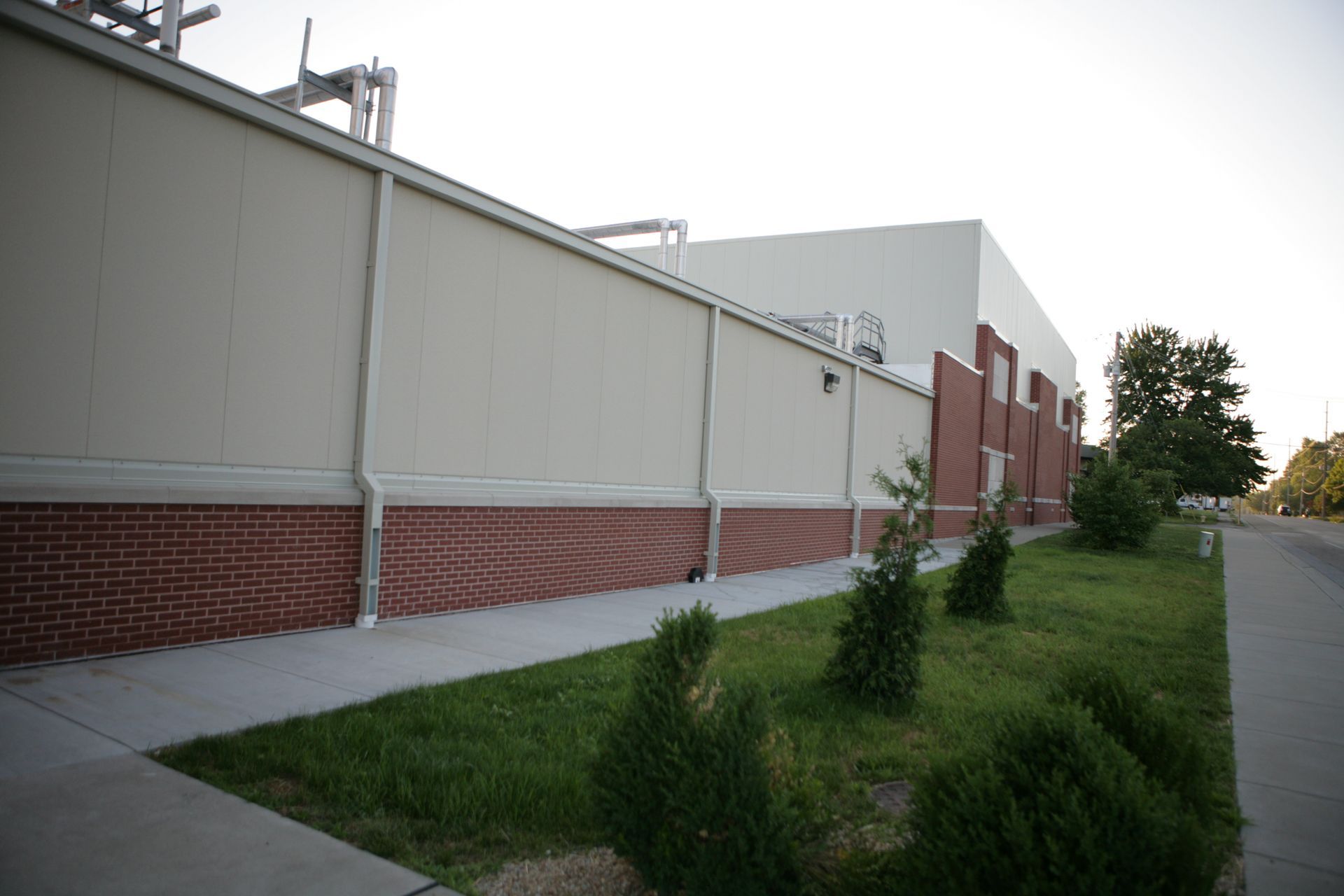 Exterior of a building with brick base, tan wall, and green lawn along a sidewalk.