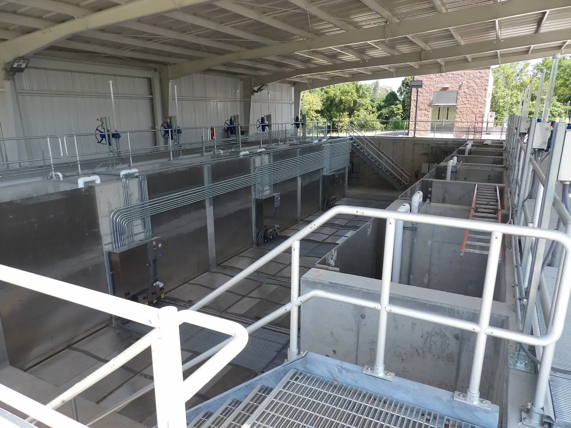 Inside a water treatment facility, tanks, pipes, and walkways under a metal roof.