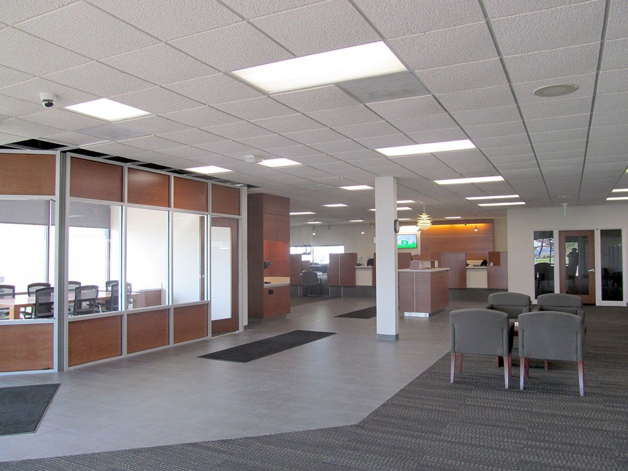 Bank lobby with seating, counters, and glass-walled offices under a drop ceiling with fluorescent lighting.