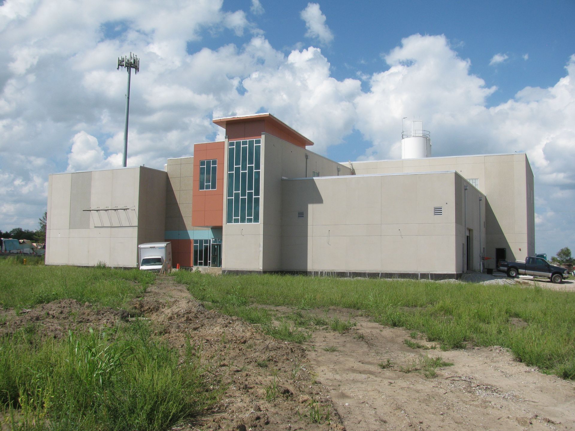 Modern building with orange accents, glass windows, and a cell tower in the background, set on a grassy hill.
