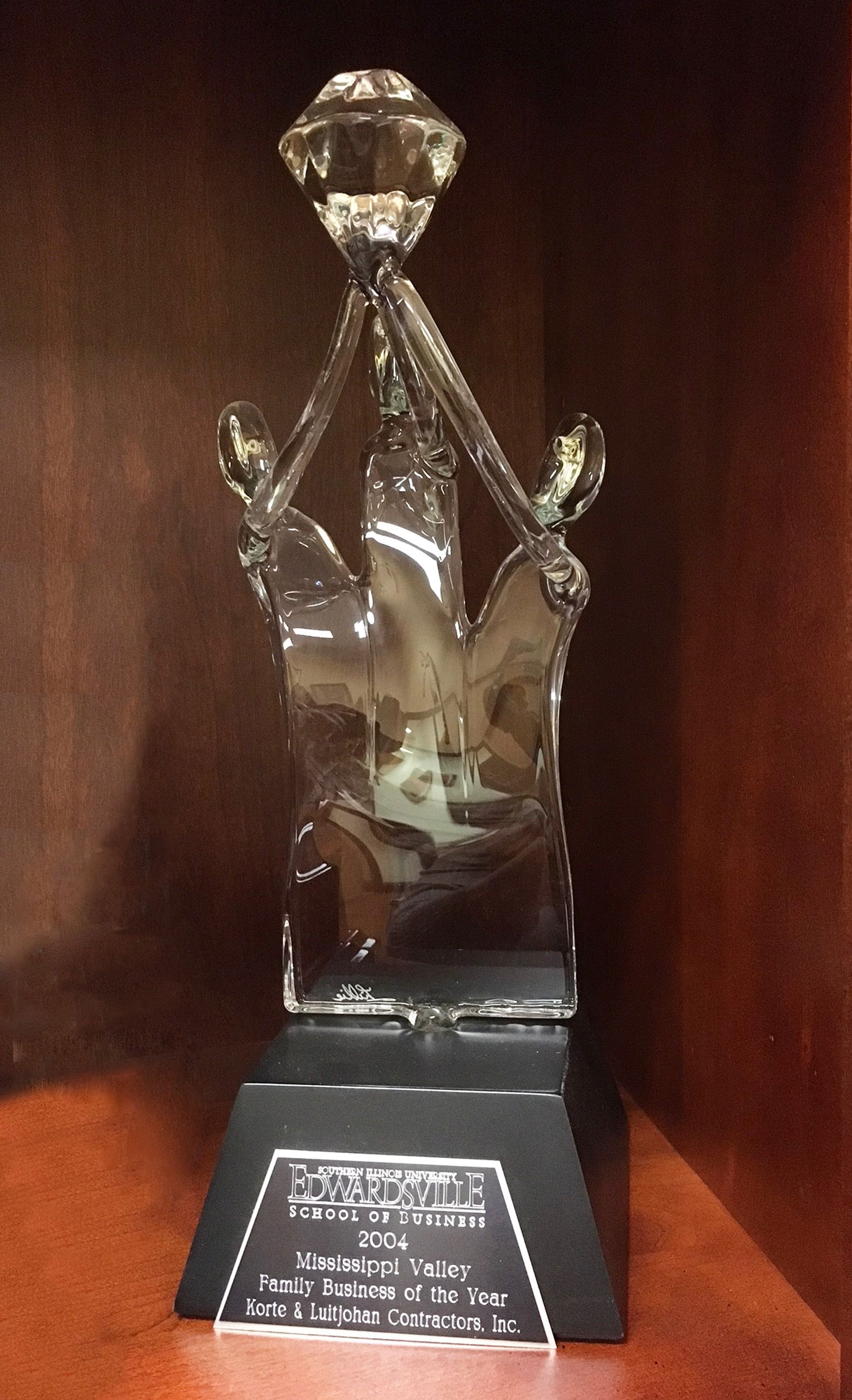 Trophy with a diamond top and hands holding it. Black base with an engraved plaque.