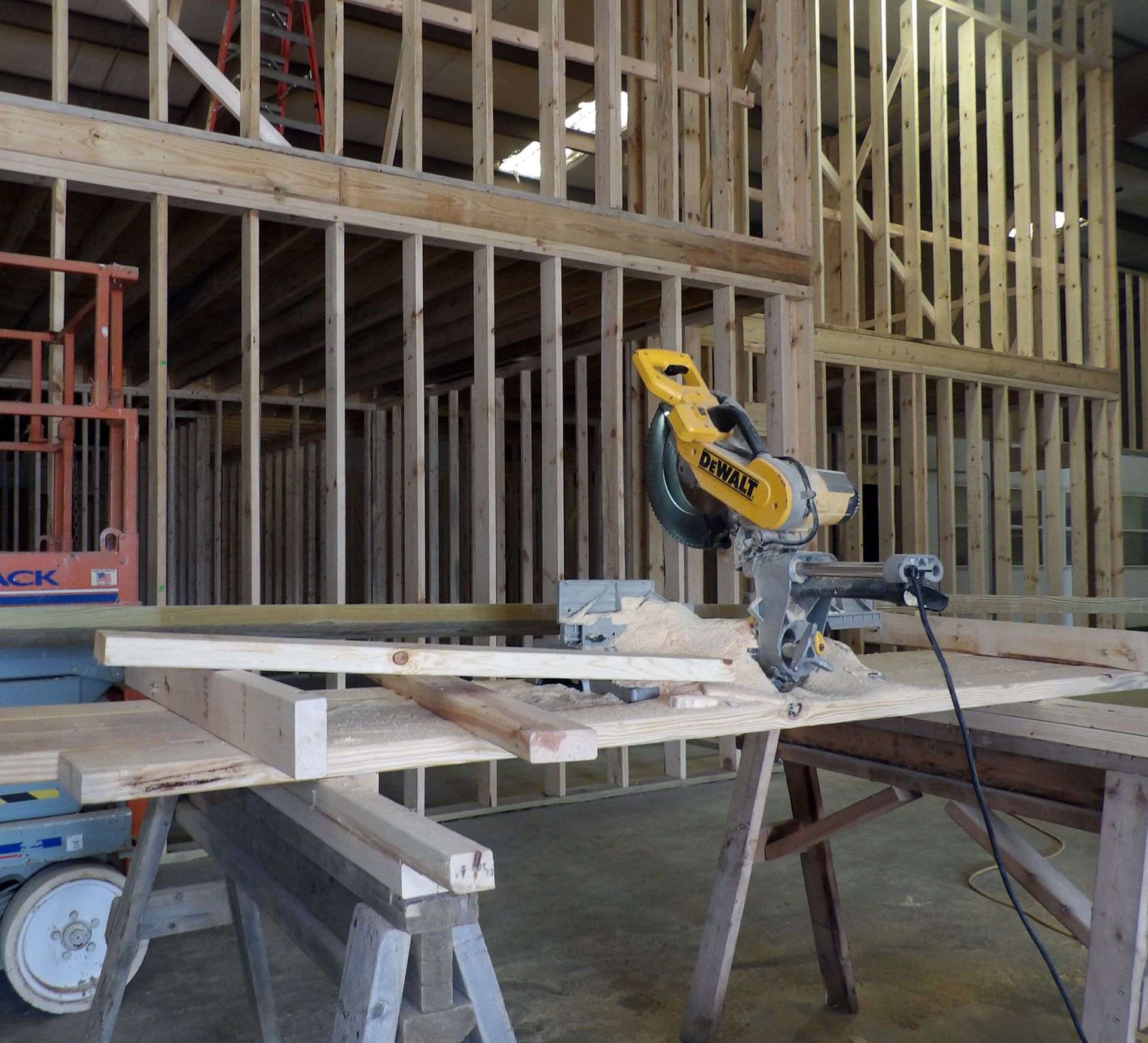 Man and woman in red shirts near a Kubota KX052 excavator. Woman sits in cab, man stands with hand on hip. Outdoors.