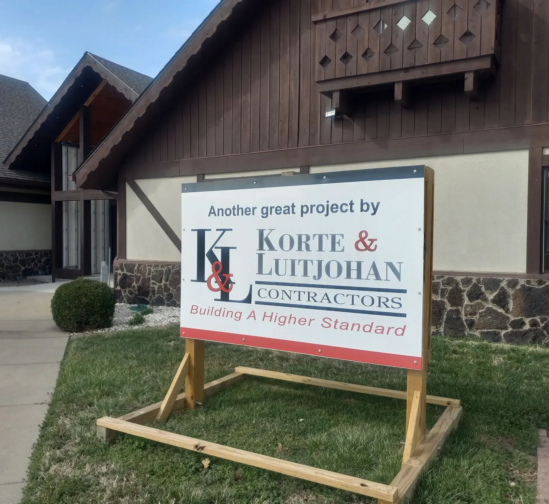 Sign for Korte & Luttjohann Contractors in front of a building with brown trim and stone accents.