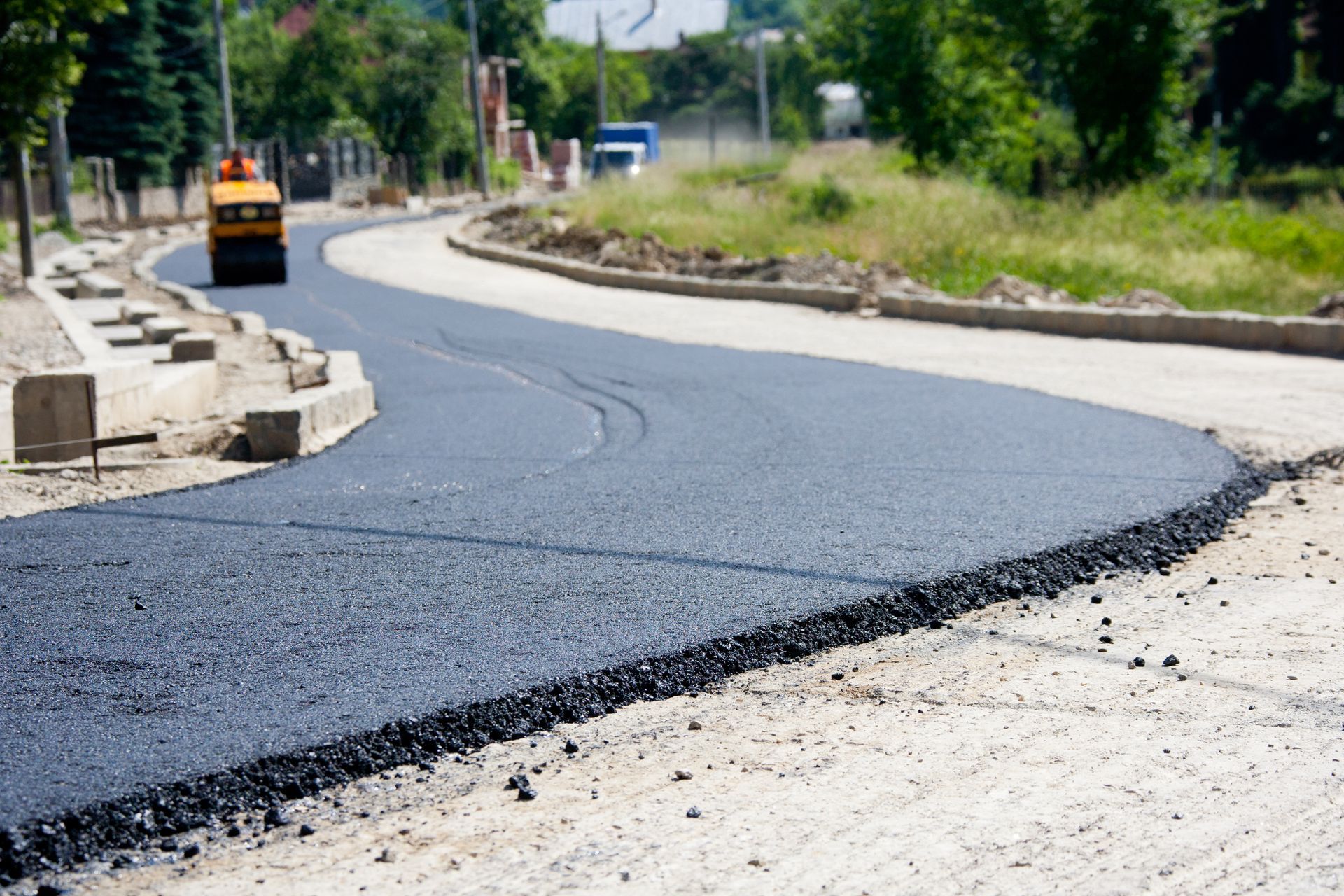 Road being paved with black asphalt; construction roller in the distance.