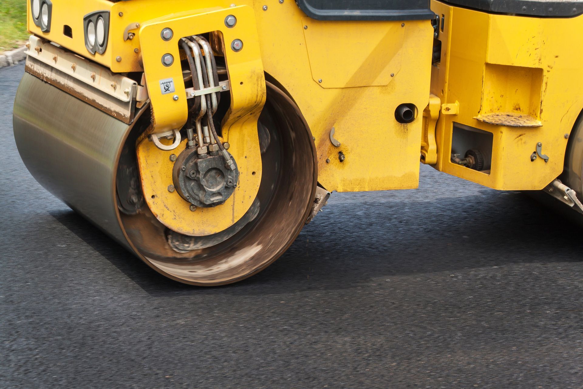Yellow road roller compacting fresh asphalt pavement.