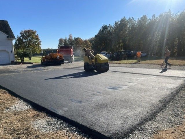 Asphalt paving a driveway. A roller compacts the fresh blacktop on a sunny day.