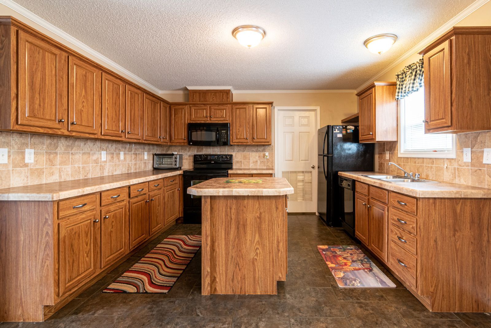 A kitchen with wooden cabinets , a black refrigerator , and a large island.