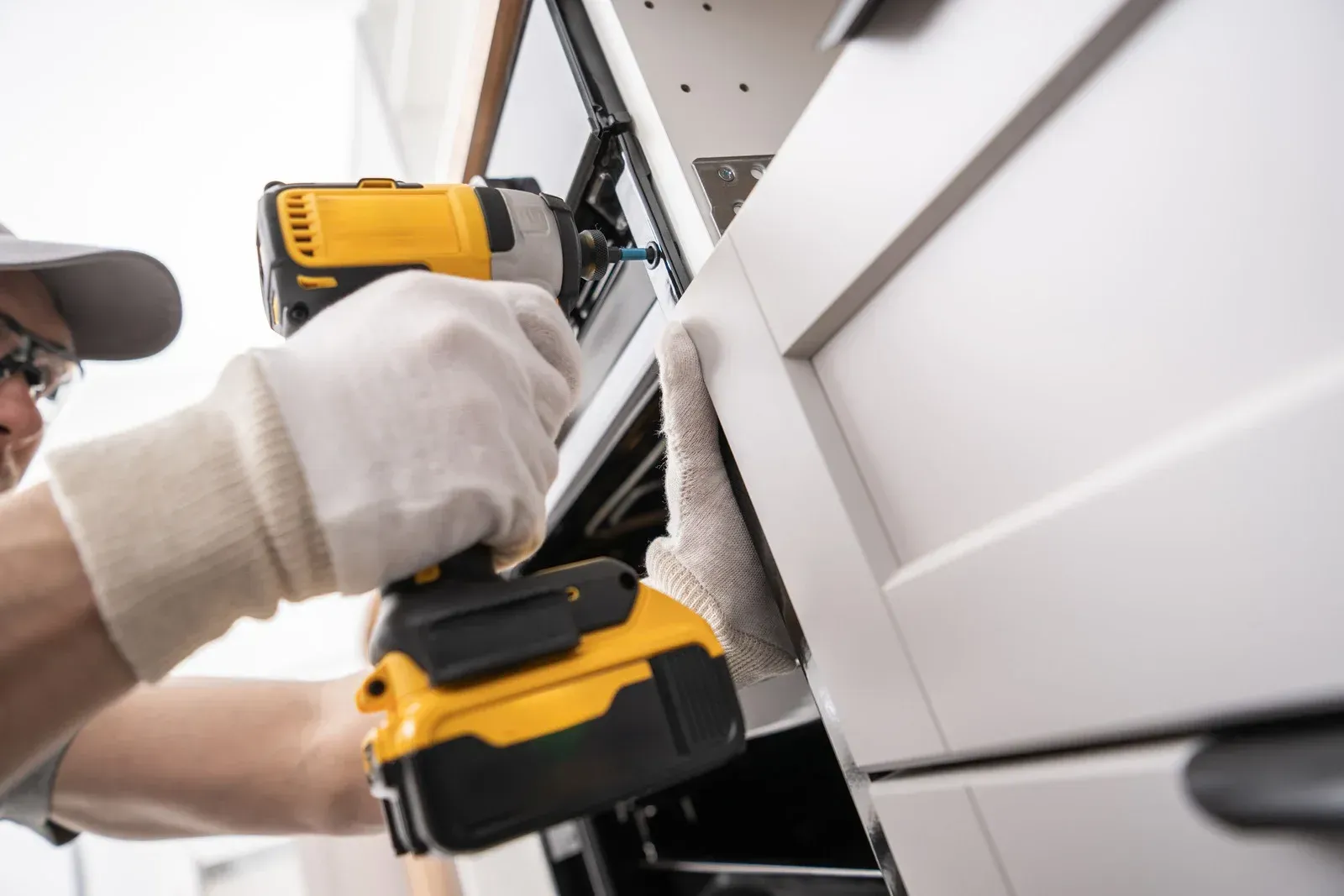 A man is working on a kitchen cabinet with a drill.