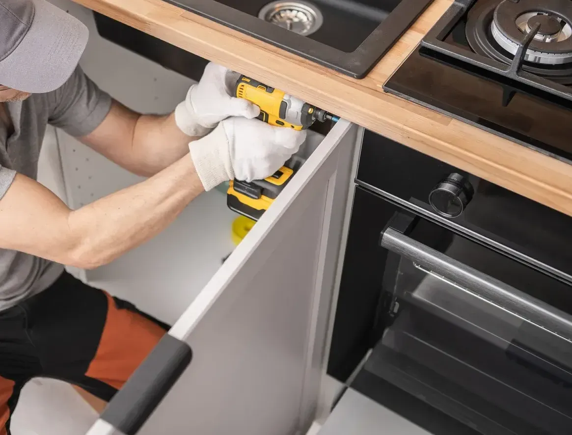 A man is fixing a sink in a kitchen with a drill.
