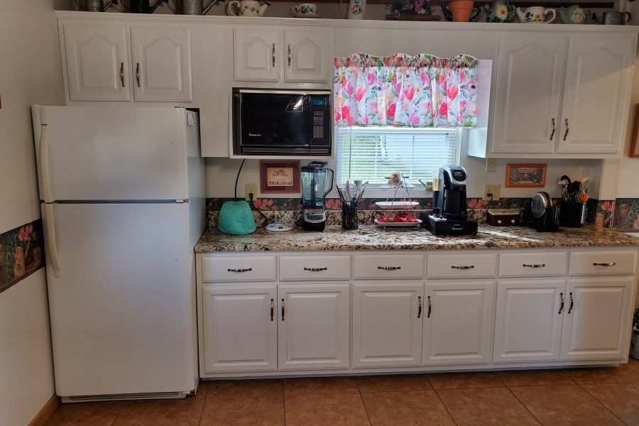 A kitchen with white cabinets , a refrigerator , a microwave , and a sink.