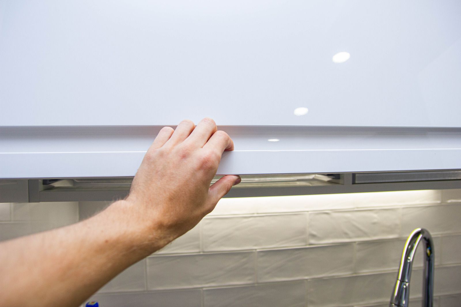 A person is opening a white cabinet door in a kitchen.