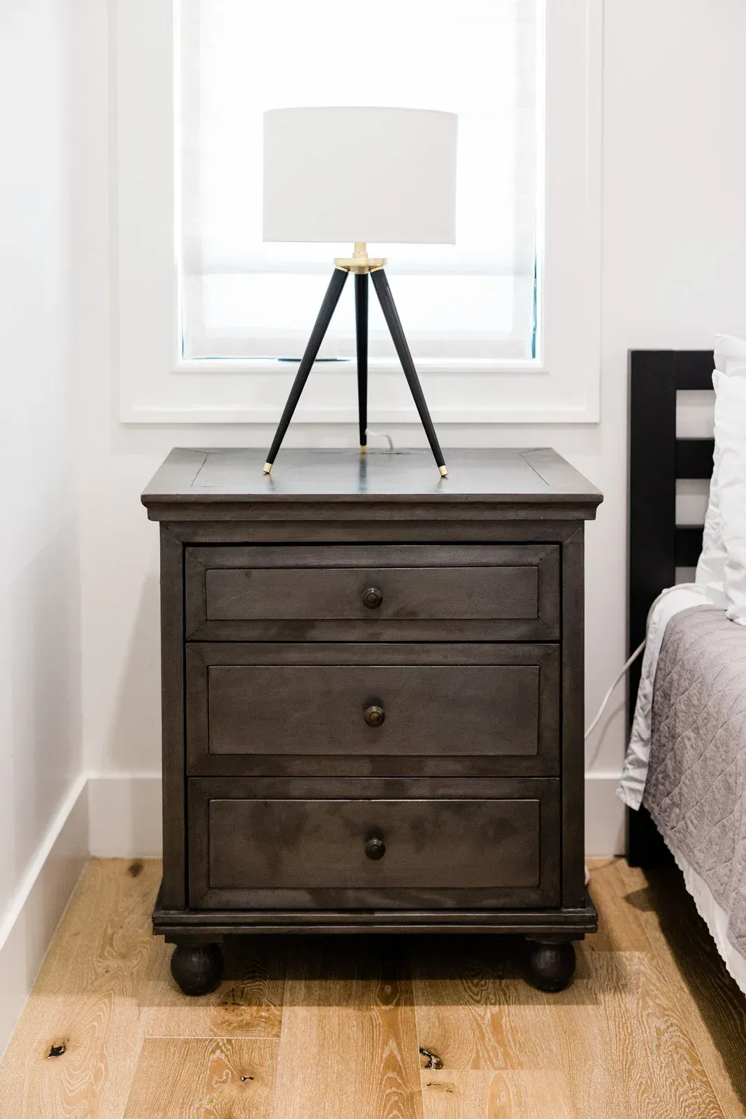 A nightstand with a lamp on top of it in a bedroom next to a bed.