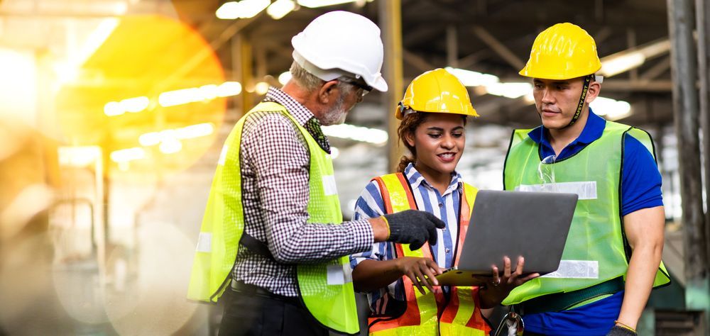 A group of construction workers are looking at a laptop in a factory.