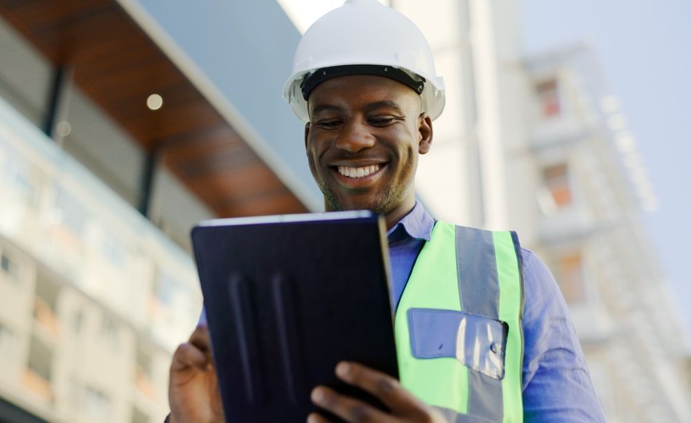 A man wearing a hard hat and safety vest is using a tablet computer.