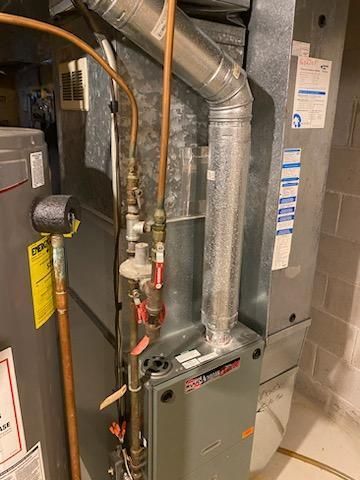 Furnace with gas and water pipes in a utility room. Gray and copper pipes against a silver metal and gray enclosure.
