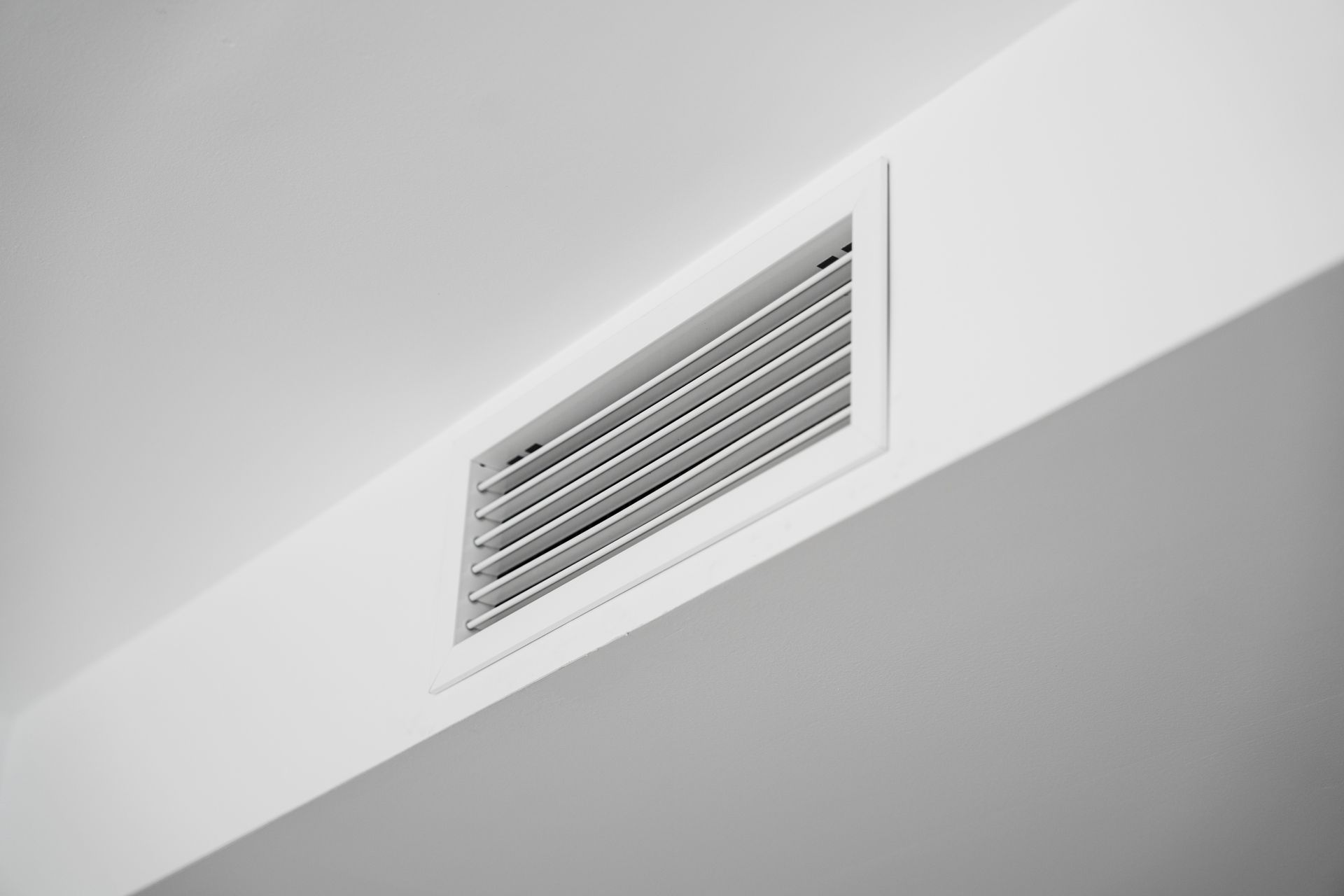 A ceiling air vent with horizontal slats on a clean white surface.