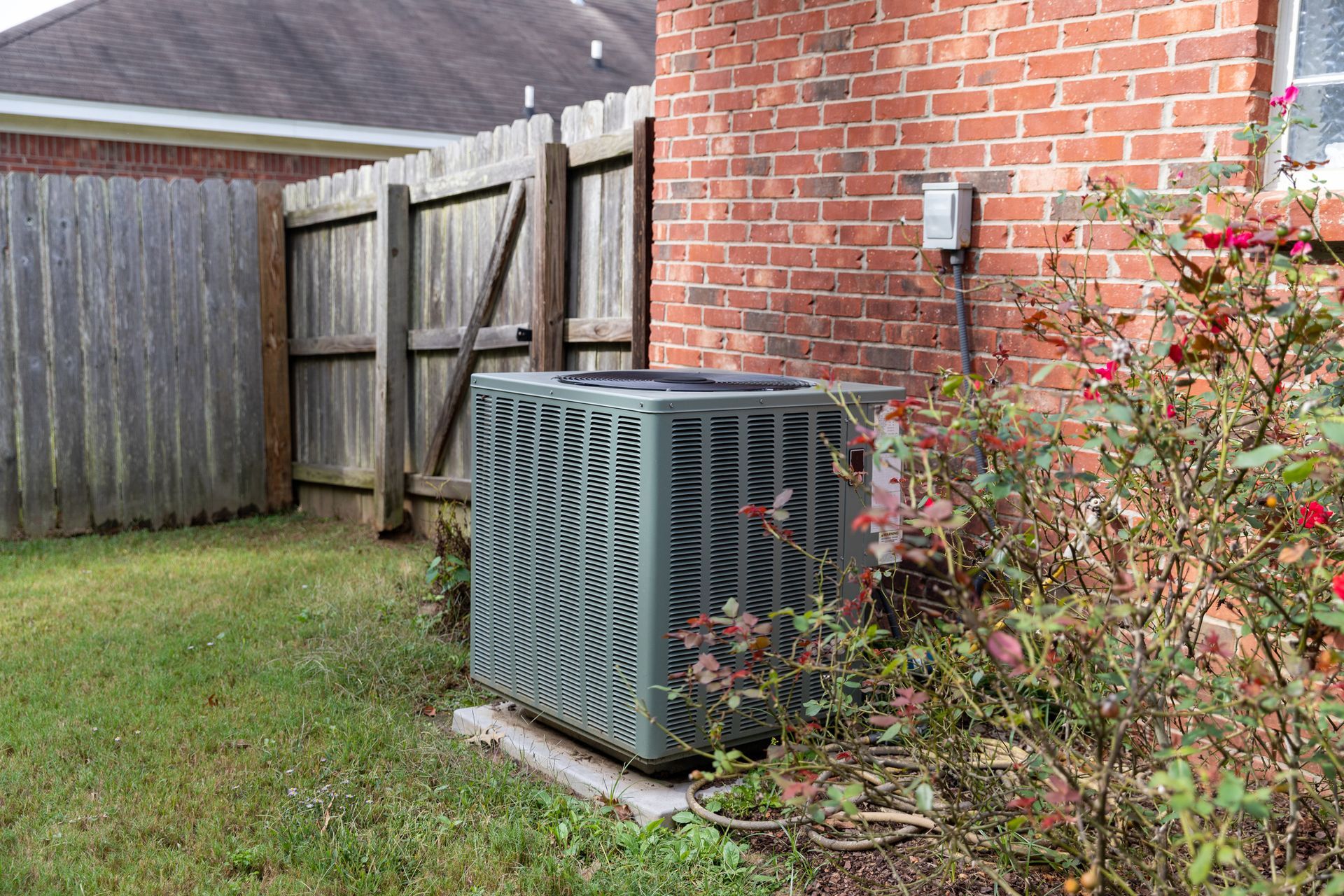 An electrician in blue overalls checks an AC unit with a multimeter.