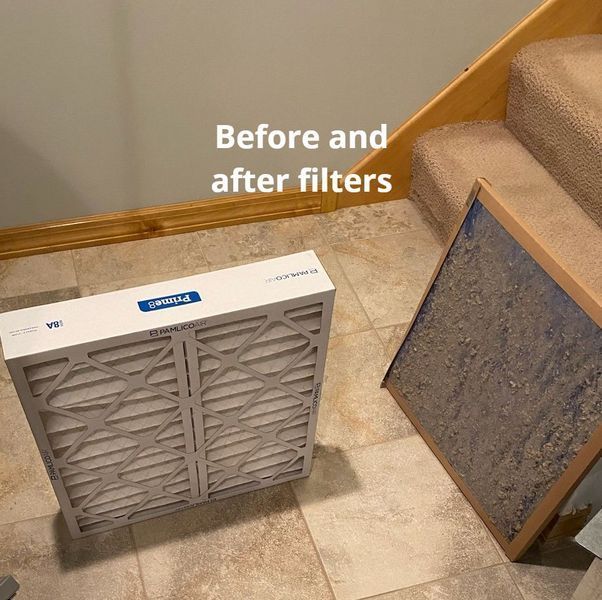 A new air filter next to a very dirty, old air filter on a tiled floor by stairs.