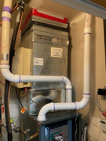 Furnace with white PVC pipes for exhaust and intake, in an indoor setting.