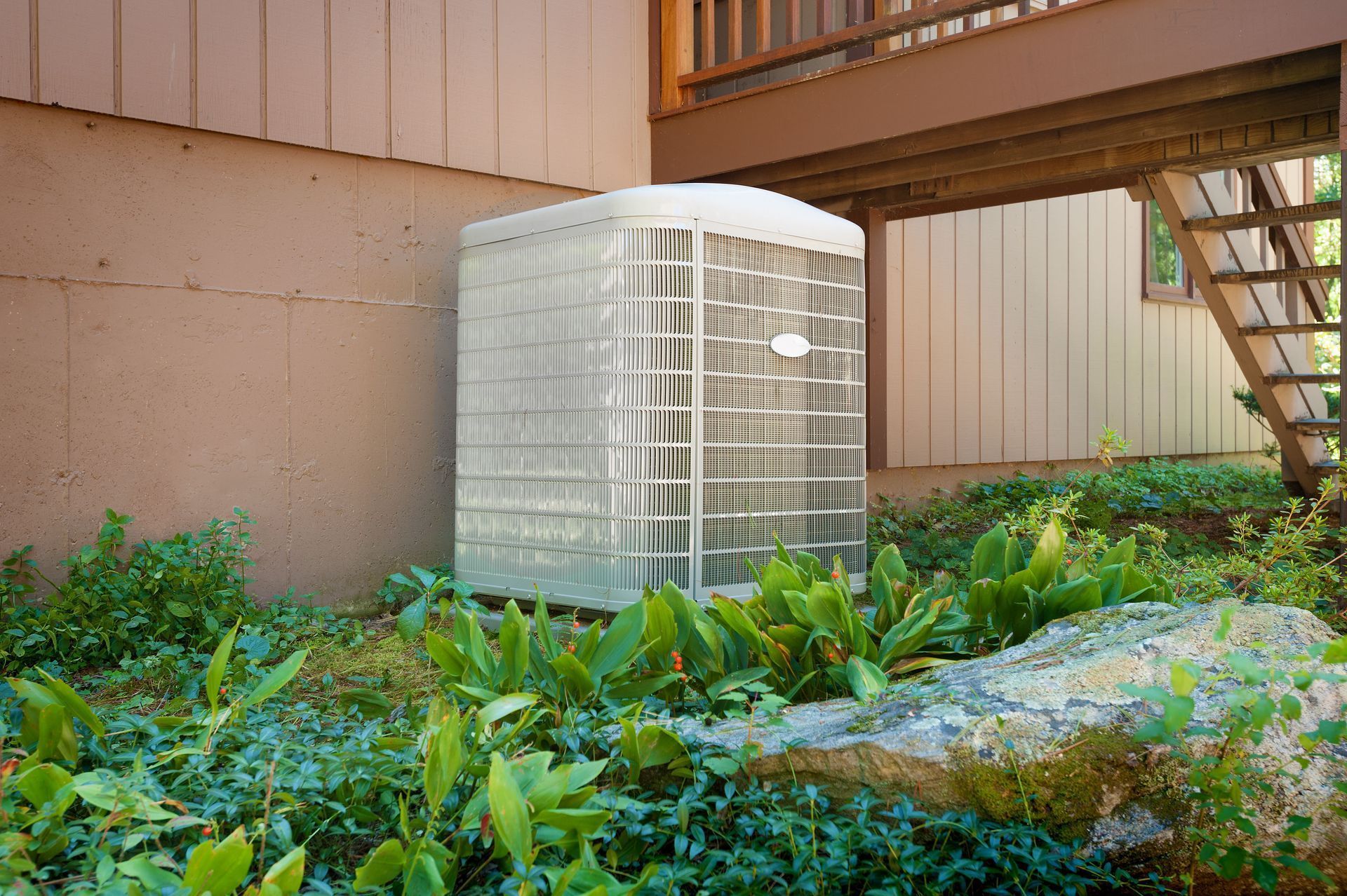 AC unit next to a house, surrounded by greenery under a deck.