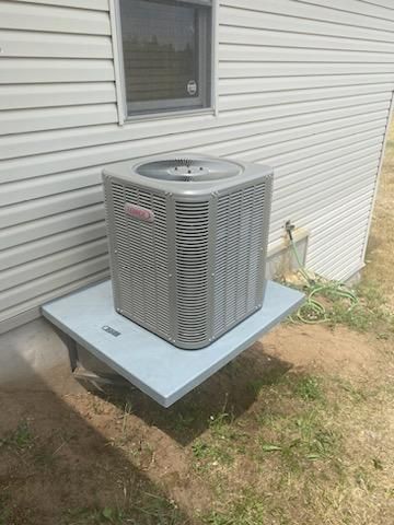 Goodman air conditioner on a gray platform beside a light gray house.