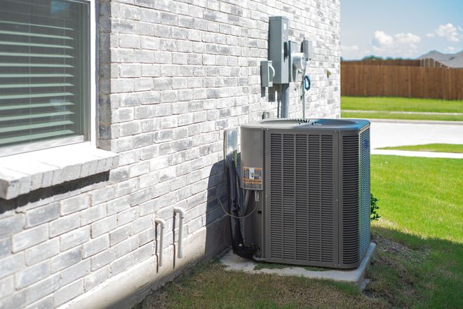 Air conditioning unit next to a brick building, on a concrete pad, in a grassy yard.