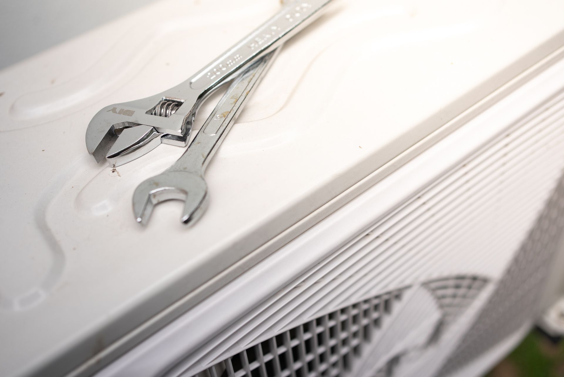 Two wrenches on top of a white air conditioning unit.