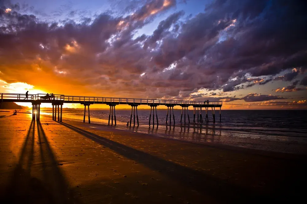 Sunset over a beach with a pier casting long shadows; orange and purple sky. — Cheyenne Drilling in Hervey Bay, QLD