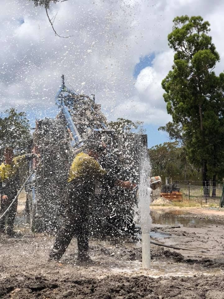 A Group of People Are Standing in the Mud With a Hose Spraying Water — Cheyenne Drilling on the Sunshine Coast, QLD