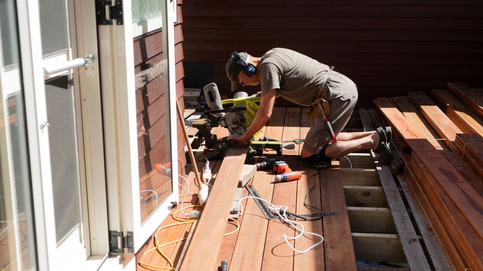 A man is working on a wooden deck with a circular saw.