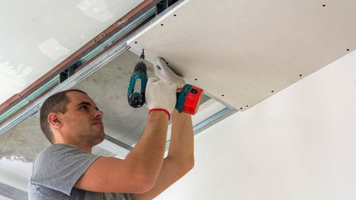 A man is installing a drywall ceiling with a drill.