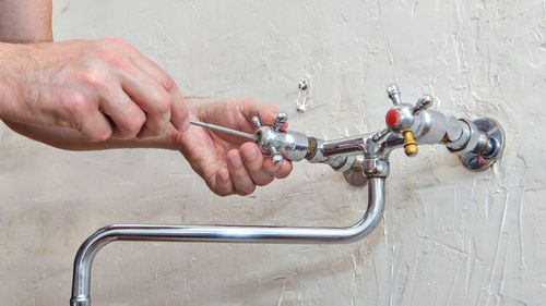 A man is fixing a faucet with a screwdriver.