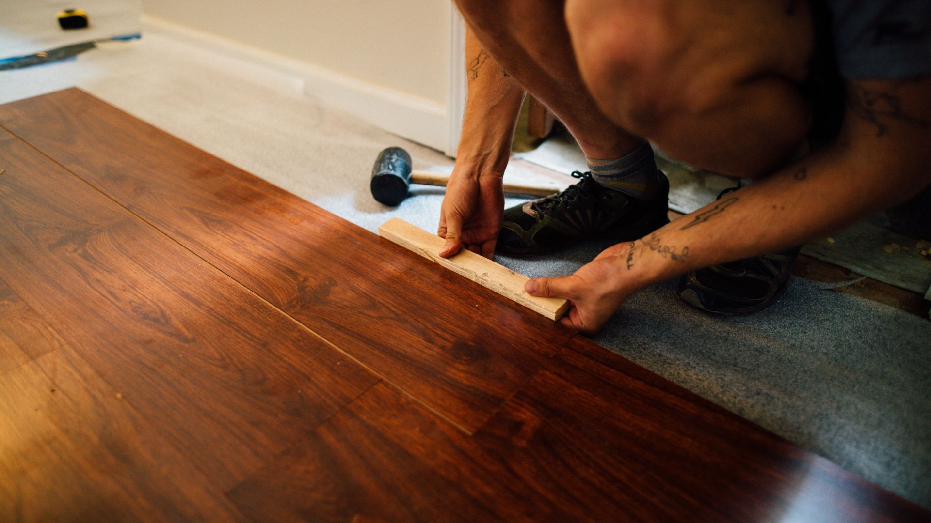A man is installing a wooden floor with a hammer.