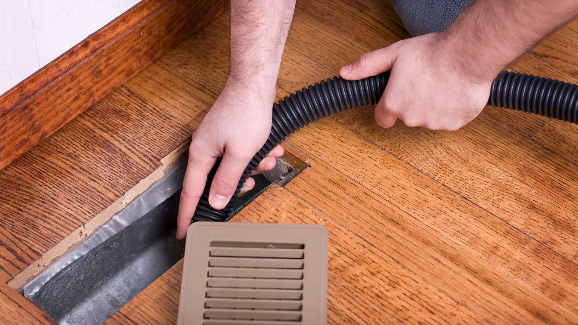 A person is using a vacuum cleaner to clean a vent on the floor.