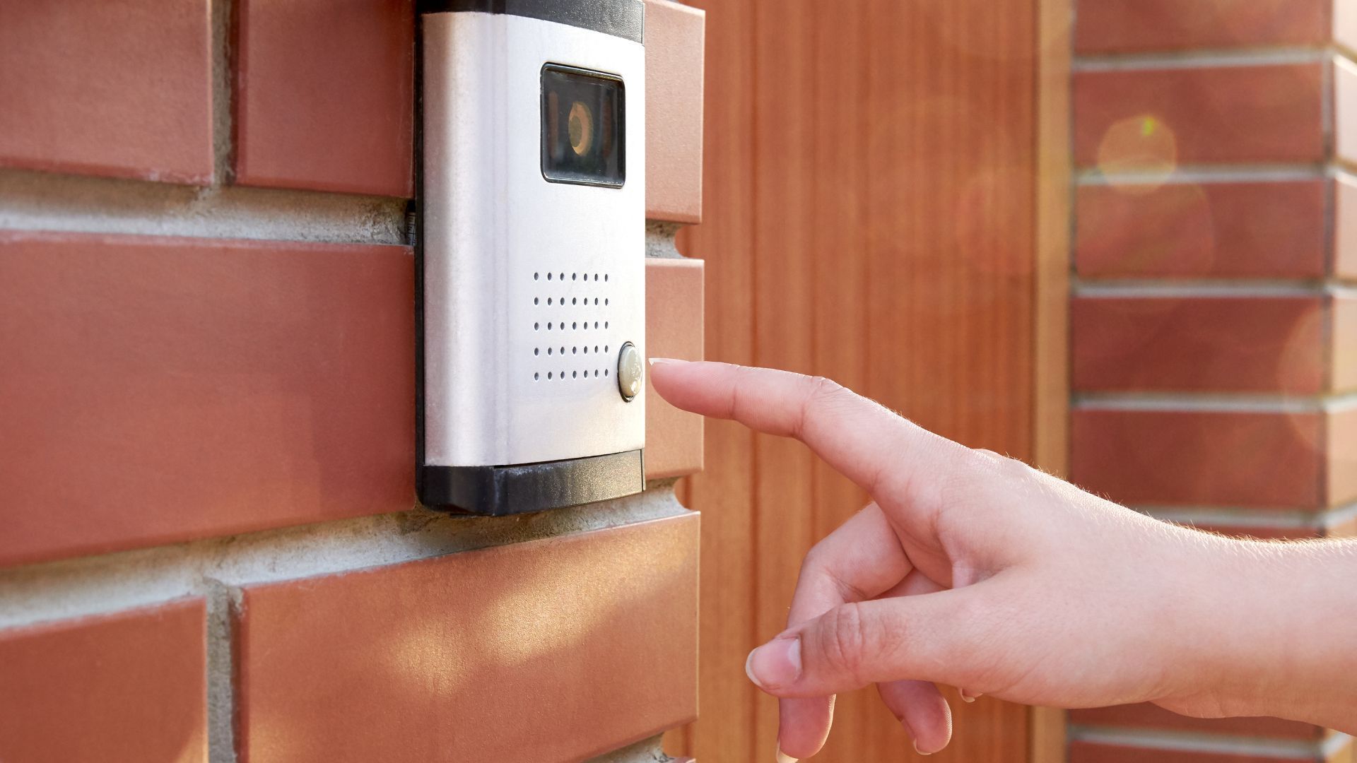 A person is pressing a doorbell on a brick wall.