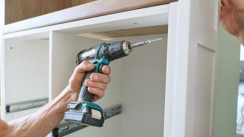 A man is using a drill to screw a screw into a cabinet.