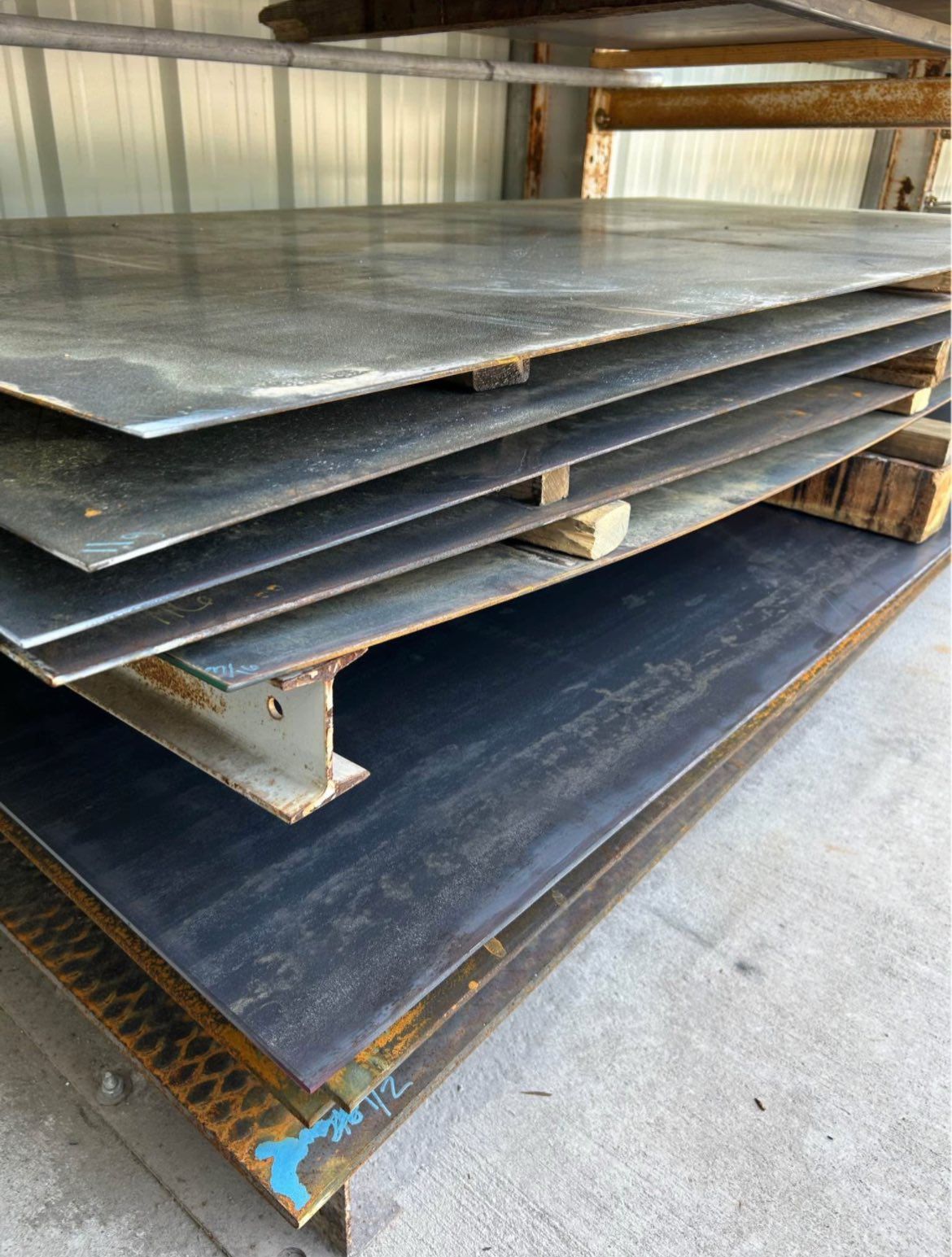 Stack of metal sheets on a metal shelf. The sheets are varying shades of gray and blue.
