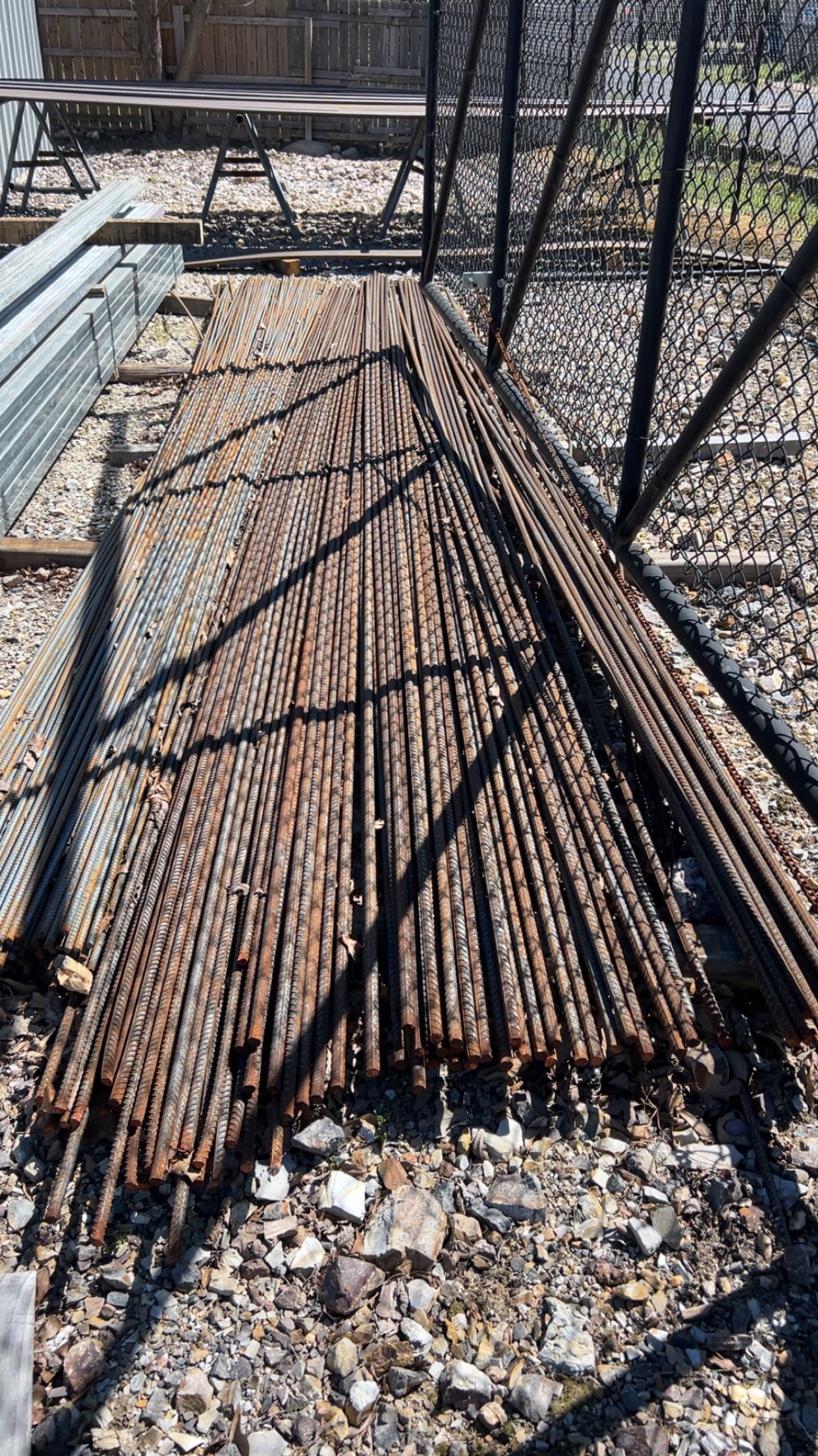 Steel railroad tracks stacked outside on gravel.