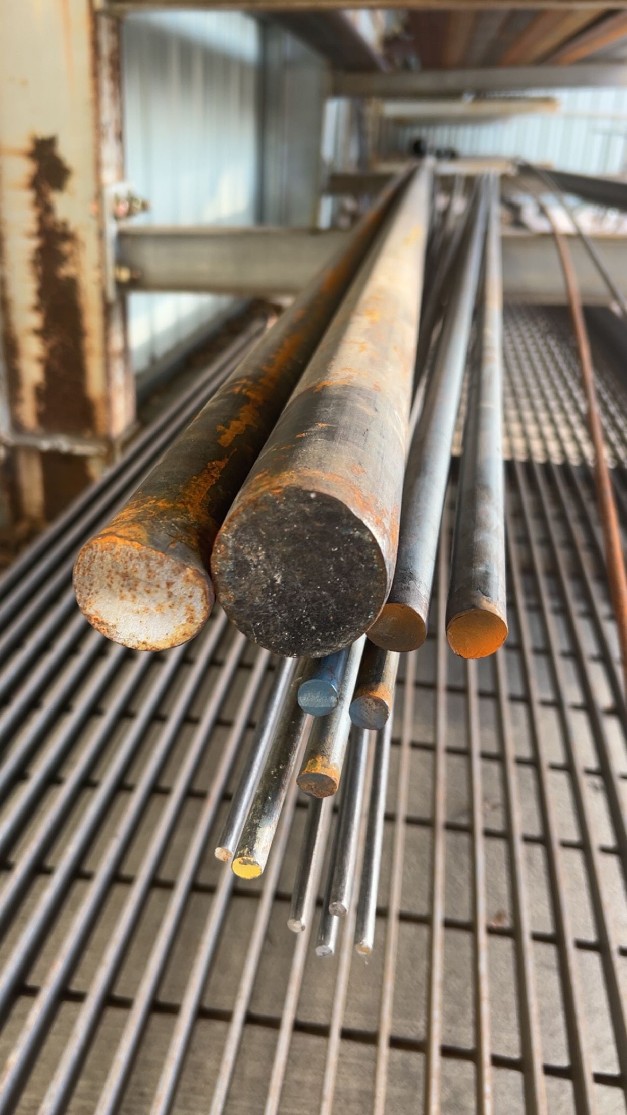 Metal rods of varying diameters and lengths rest on a metal grid shelf.