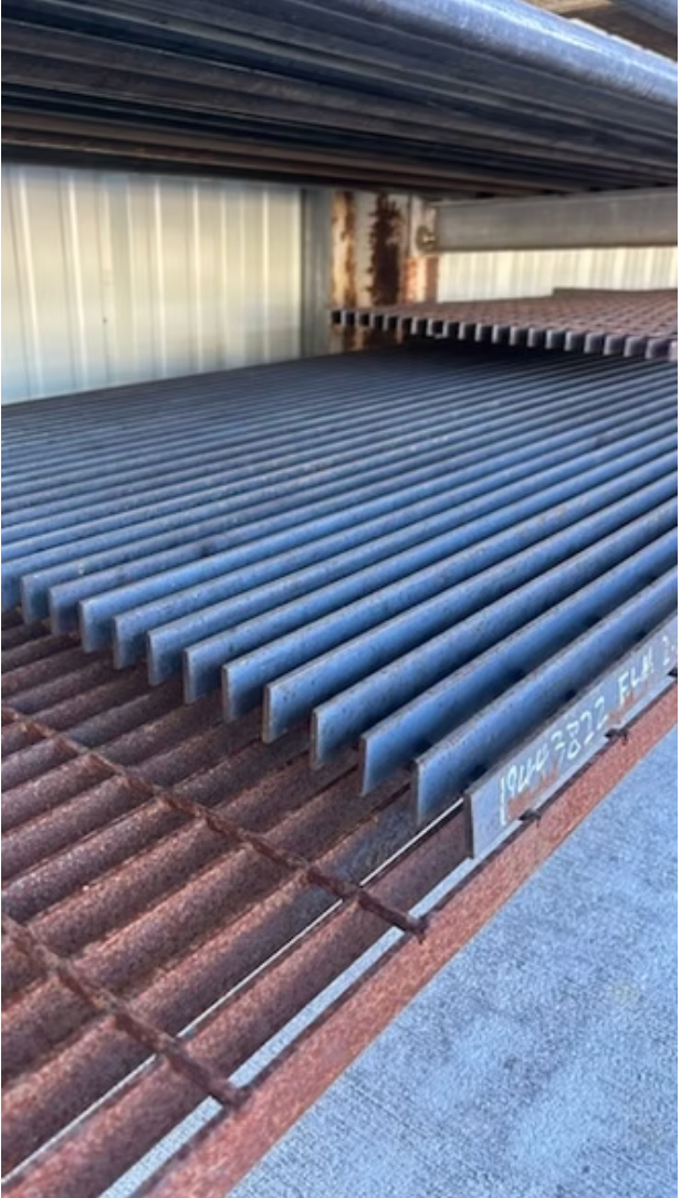 Metal beams of various types and lengths on a gravel surface.