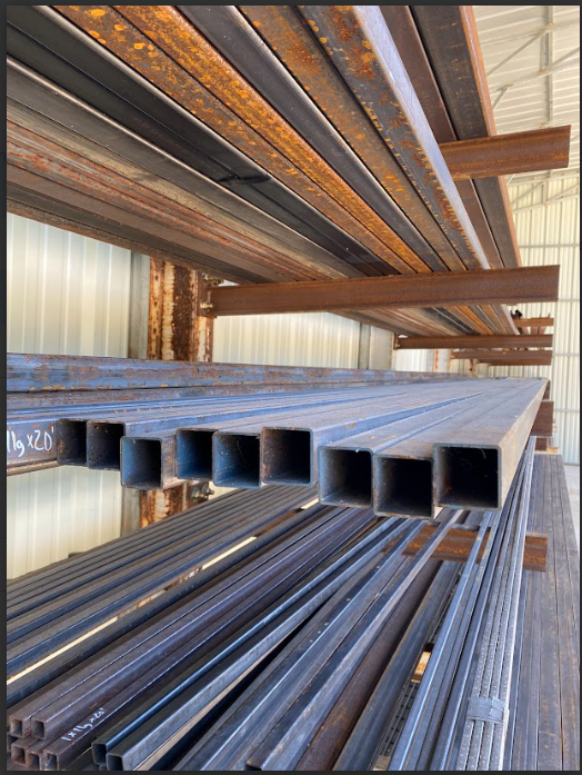 Brown metal beams stacked on a wooden pallet, with chains attached. Outdoors, sunny.