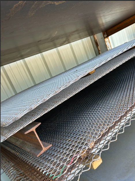 Sheets of expanded metal stacked with an I-beam in a metal storage area.