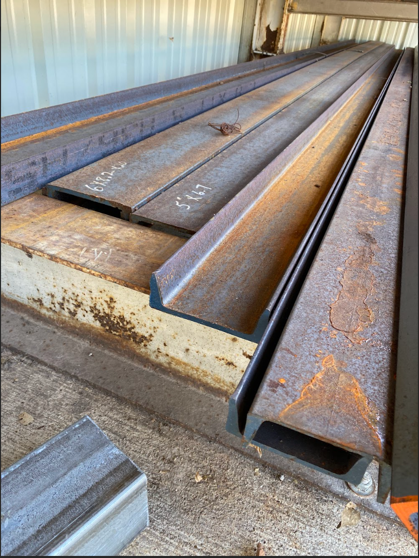 Metal beams stacked on a rust-covered platform, inside a building.