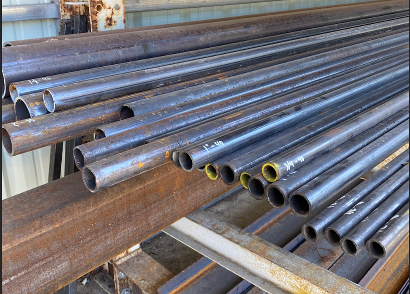 Pile of dark metal tubes on a rusty metal rack, some with yellow interiors.