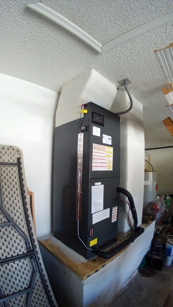 A black air conditioner is sitting on top of a wooden shelf in a garage.