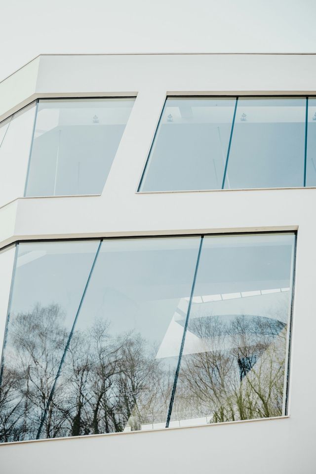 A white building with a lot of windows and trees reflected in the windows.