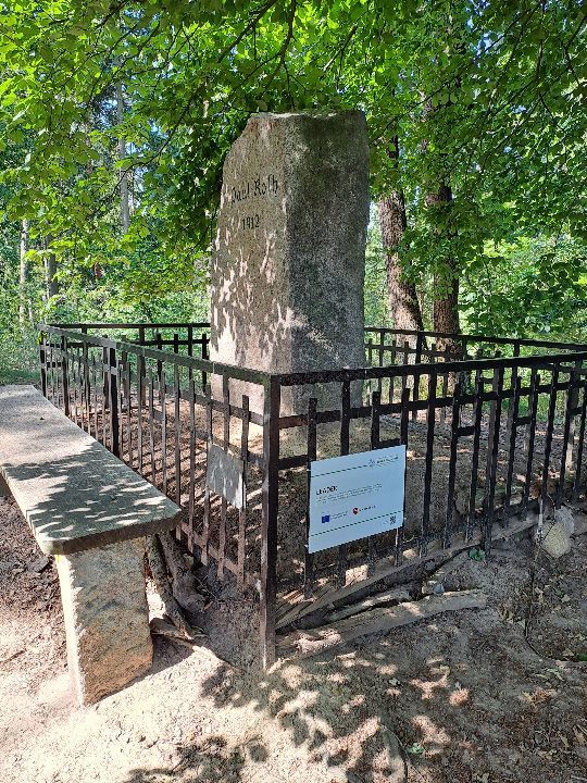 Granitstein mit Widmung von einem eisernen Schmuckzaun umgeben und mit der Förderplakette LEADER