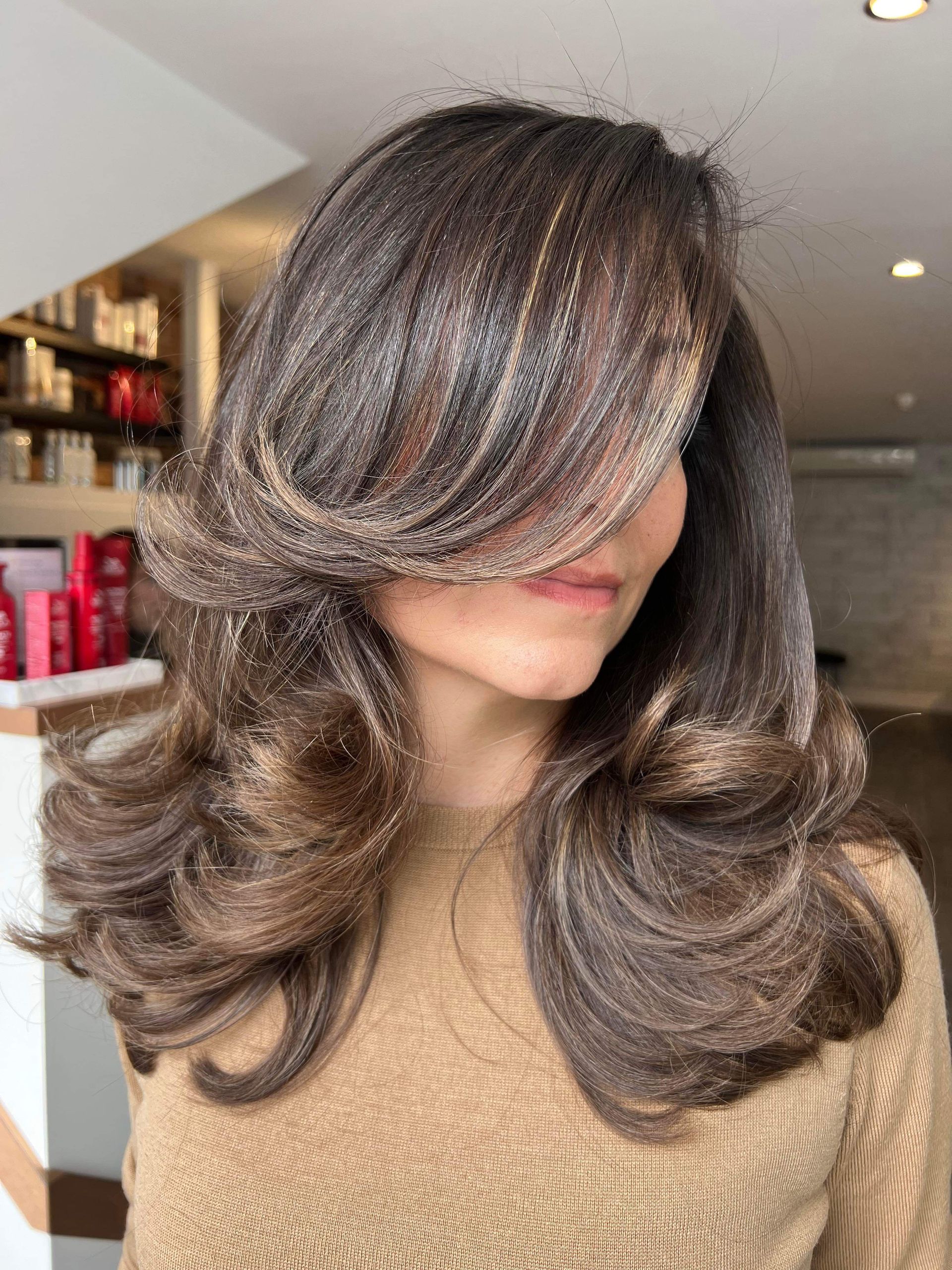A woman with long brown hair is covering her face with her hair.